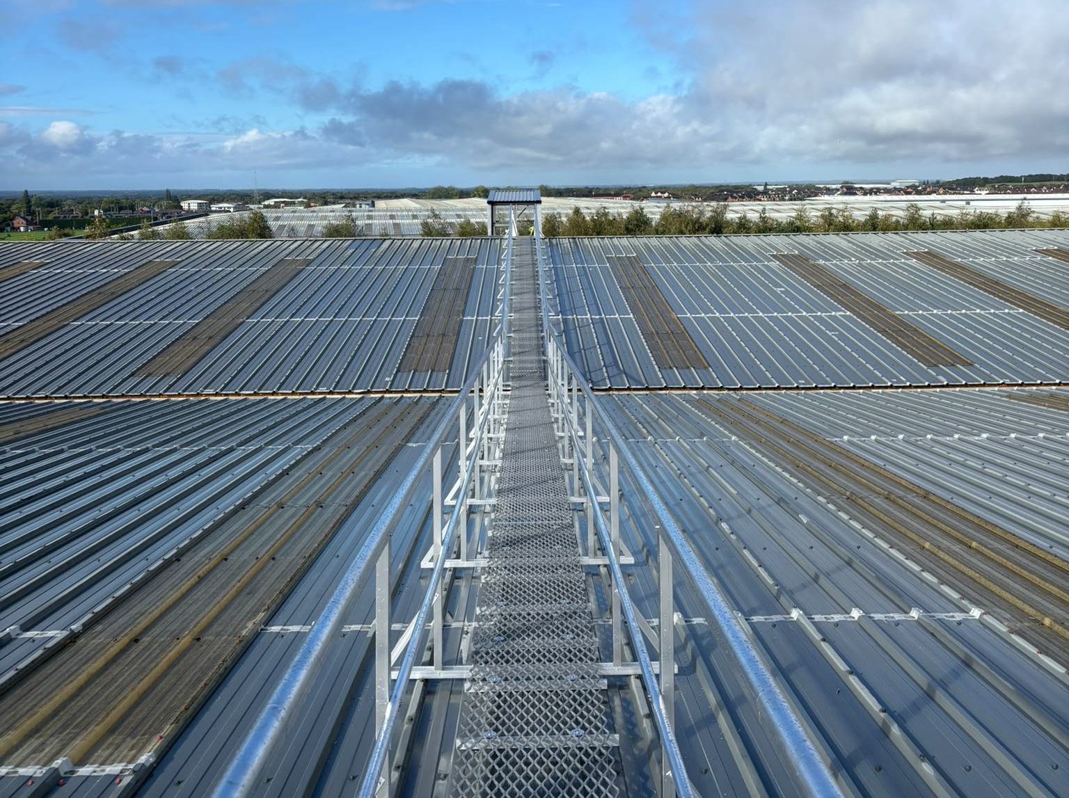 Mesh walkway with handrail on both sides crossing a large industrial roof, installed by AdSafe