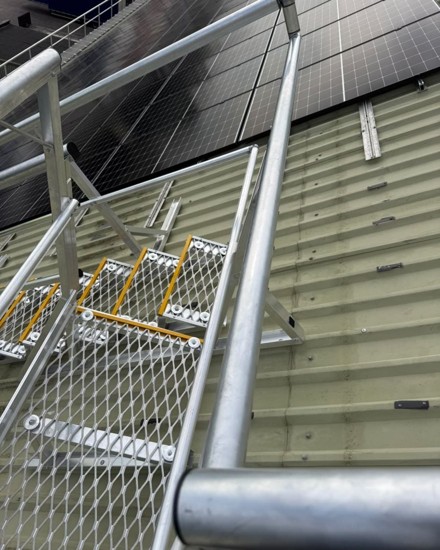 Aluminium roof stair with mesh treads and handrails beside a solar array on a pitched roof