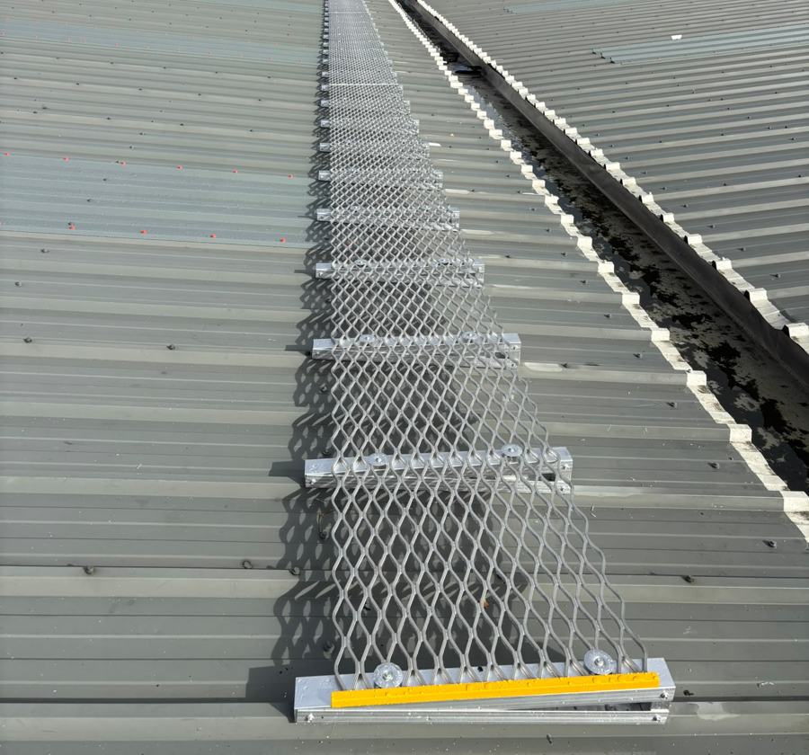 Mesh walkway with yellow nosing fixed to a profiled roof beside a valley gutter