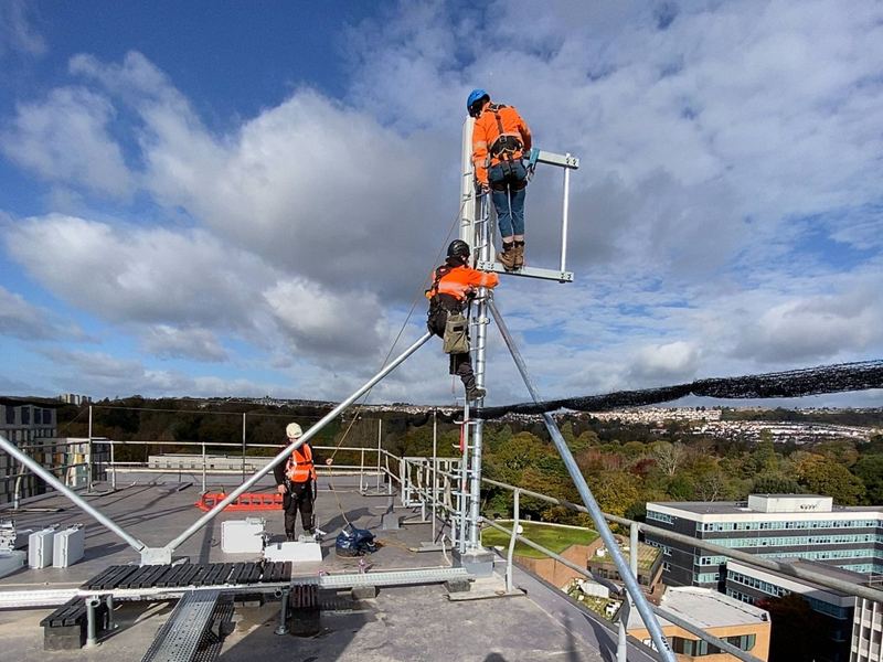 Two AdSafe engineers in harnesses climbing a new rooftop antenna pole