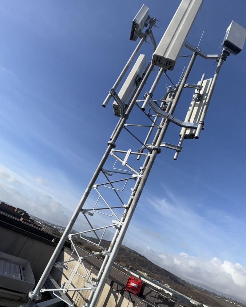 Lattice antenna pole with three antennas on a rooftop against blue sky