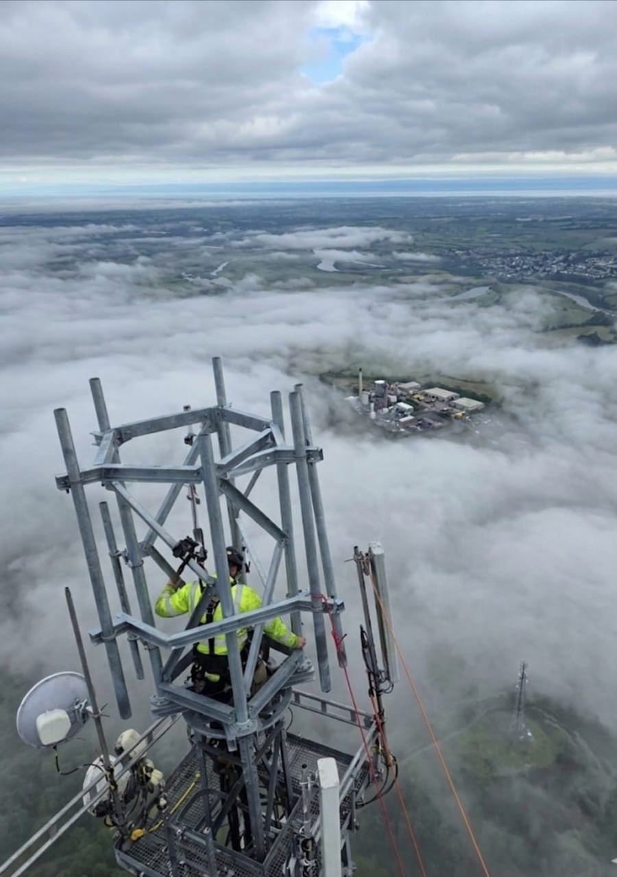 Engineer working at the top of a telecoms tower above low cloud