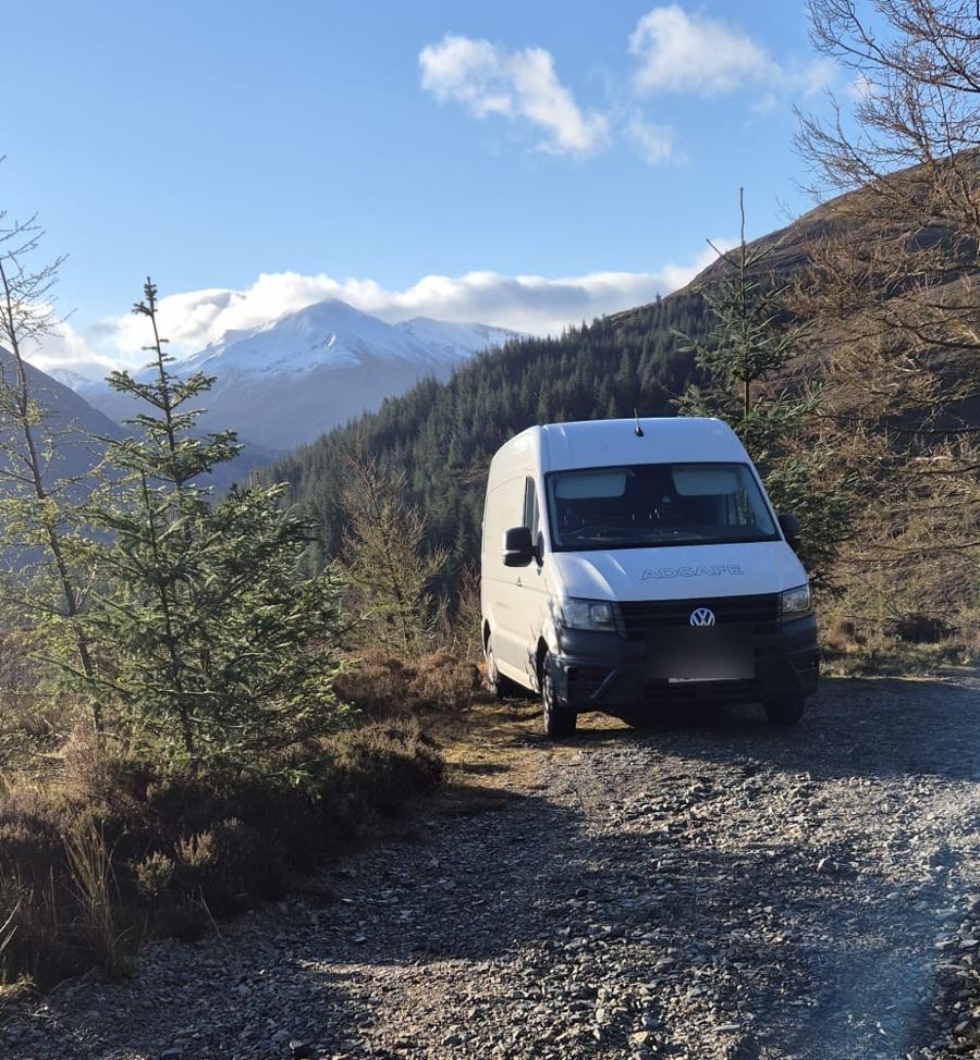 White AdSafe van parked on a mountain track with snow-capped peaks behind